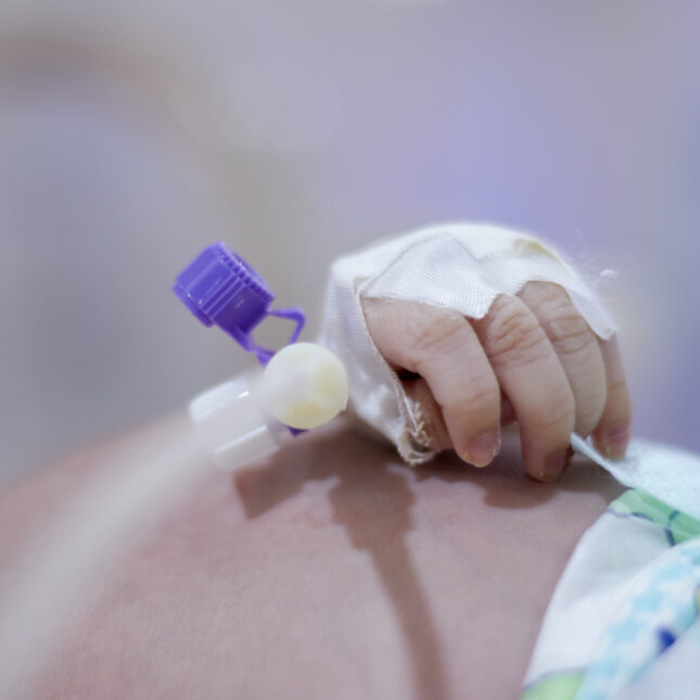 A stock photo of a baby's hand with medical bracelet attached, in a NICU bed