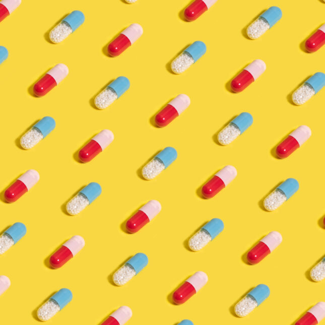 Stock photo of blue and red pills arranged in a pattern on a bright yellow background