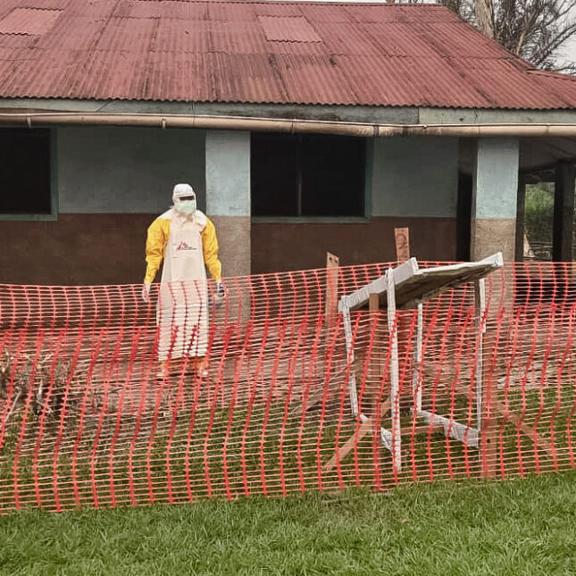 a man wearing protective clothing stands outside an Ebola treatment center in the remote Bulape Health Zone, Kasaï province, the Democratic Republic of Congo