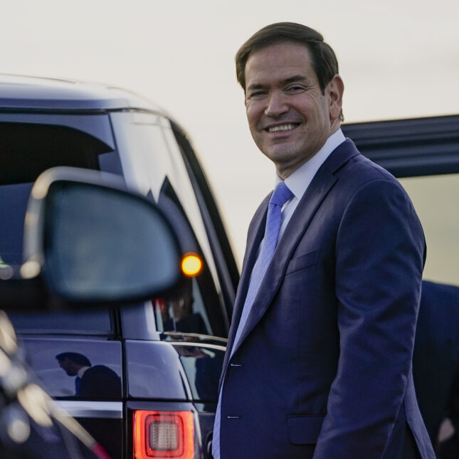 Secretary of State Marco Rubio smiles as he prepares to enter a vehicle upon arrival at London Stansted Airport